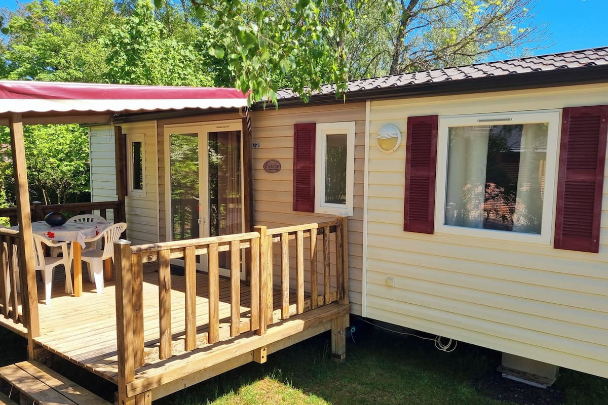 Una casa móvil con terraza de madera, un porche cubierto y una pequeña zona de estar al aire libre.