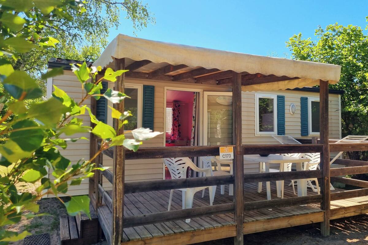 Una casa móvil con un porche cubierto, mobiliario exterior y una puerta visible que da a un espacio interior.