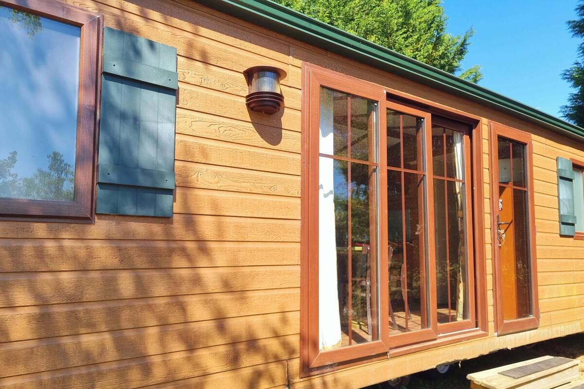 Una cabaña de madera con ventanas amplias, techo verde y una terraza de madera.