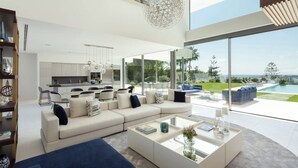 Ein modernes Wohnzimmer mit einer großen Couch, einem Couchtisch und Blick auf Pool und Garten.