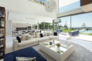 Ein modernes Wohnzimmer mit einer großen Couch, einem Couchtisch und Blick auf Pool und Garten.