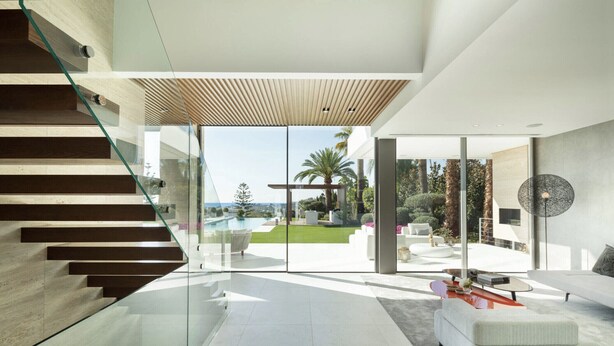 Ein modernes Interieur mit einer Treppe, einer Glastür zum Pool und einem Wohnbereich mit Sofa und Couchtisch.