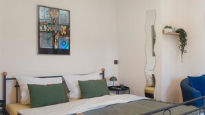 Une chambre moderne avec un cadre de lit en métal, une grande peinture abstraite, une table de chevet avec une lampe et un miroir au mur.