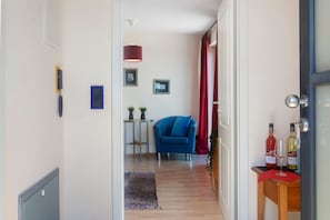 Ein Zimmer mit blauem Sessel, einem kleinen Tisch mit Pflanze, rotem Vorhang und zwei Flaschen auf einem Holznachttisch.
