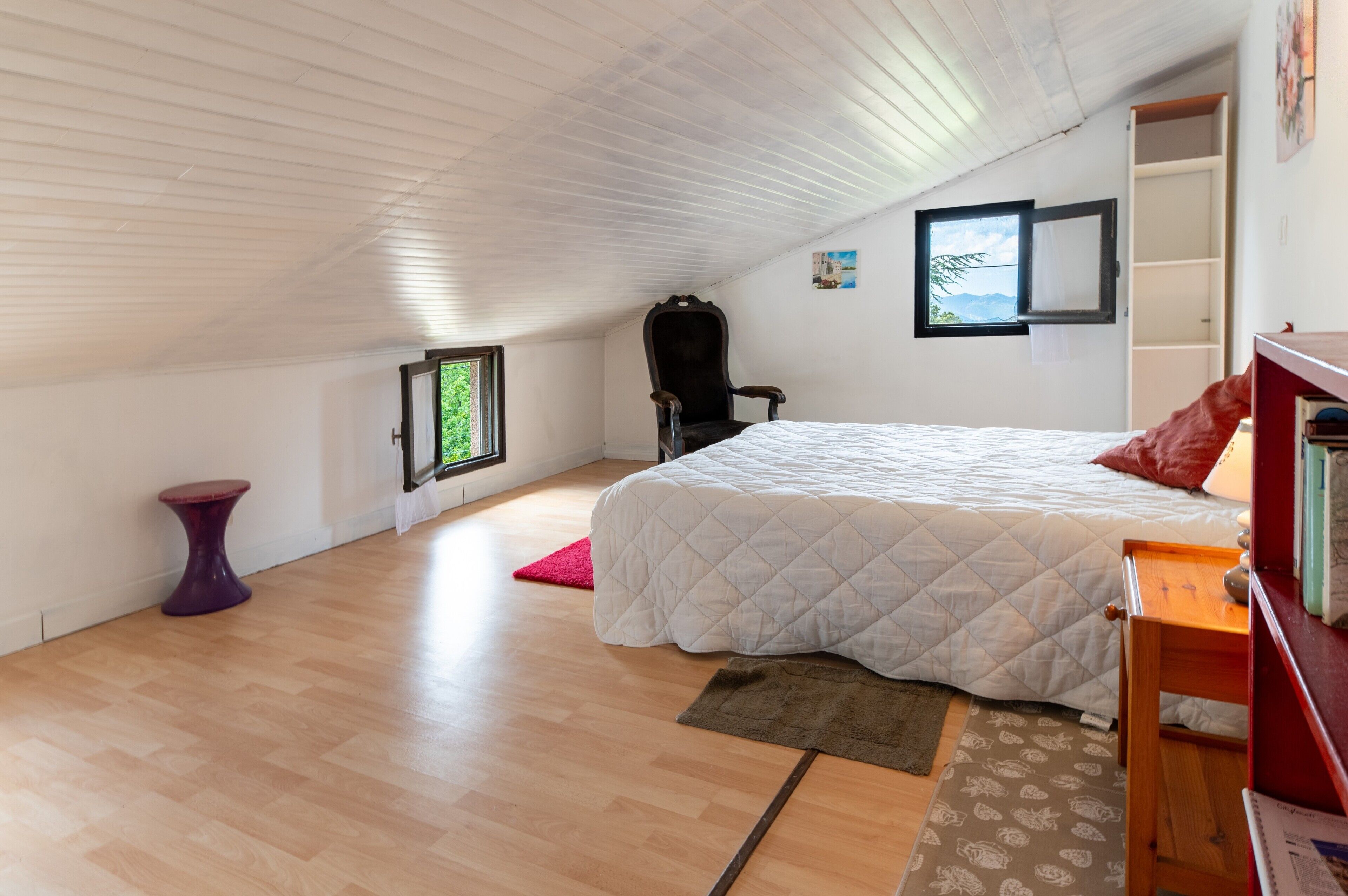 A bedroom with a bed, a chair, a small table, a window, and a bookshelf.