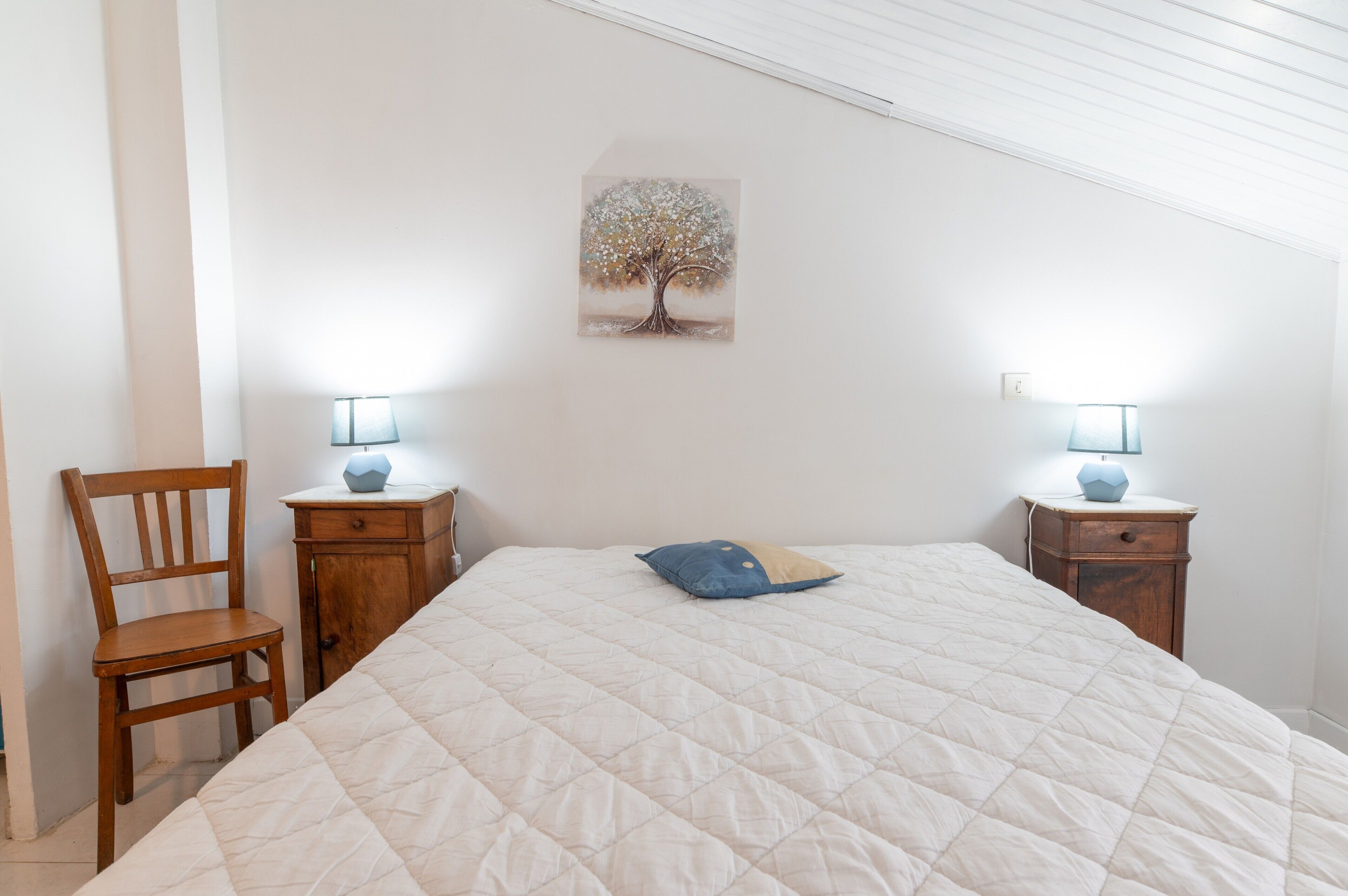 Ein Schlafzimmer mit einem großen Bett, zwei Nachttischen mit Lampen, einem Sessel und einem Wandbild.