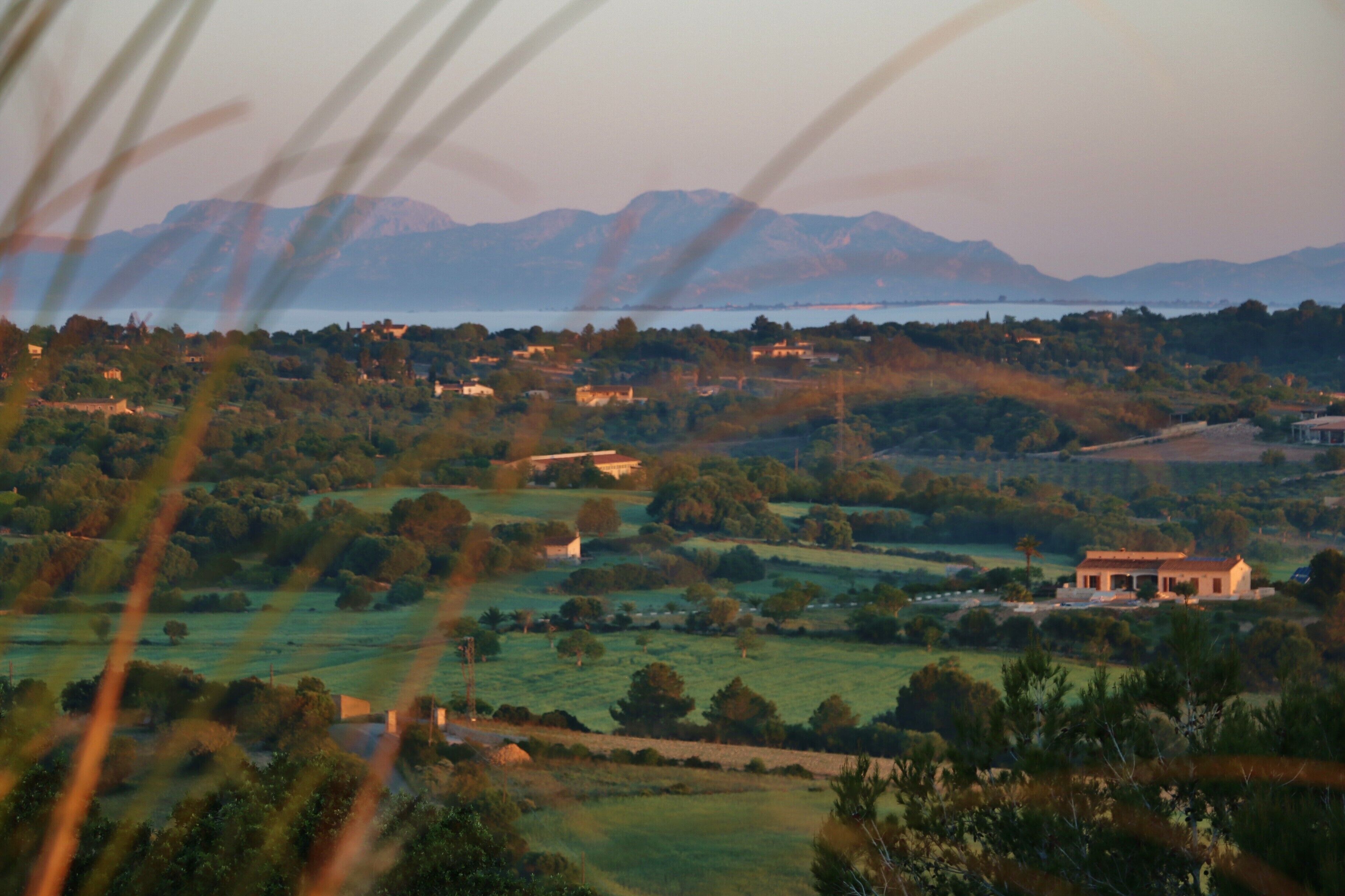 Paisagem rural com montanhas ao fundo, um corpo d'água e algumas construções dispersas.