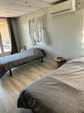 Une chambre d’hôtel avec deux lits, une fenêtre avec des rideaux, un appareil de climatisation et un petit panier en osier.