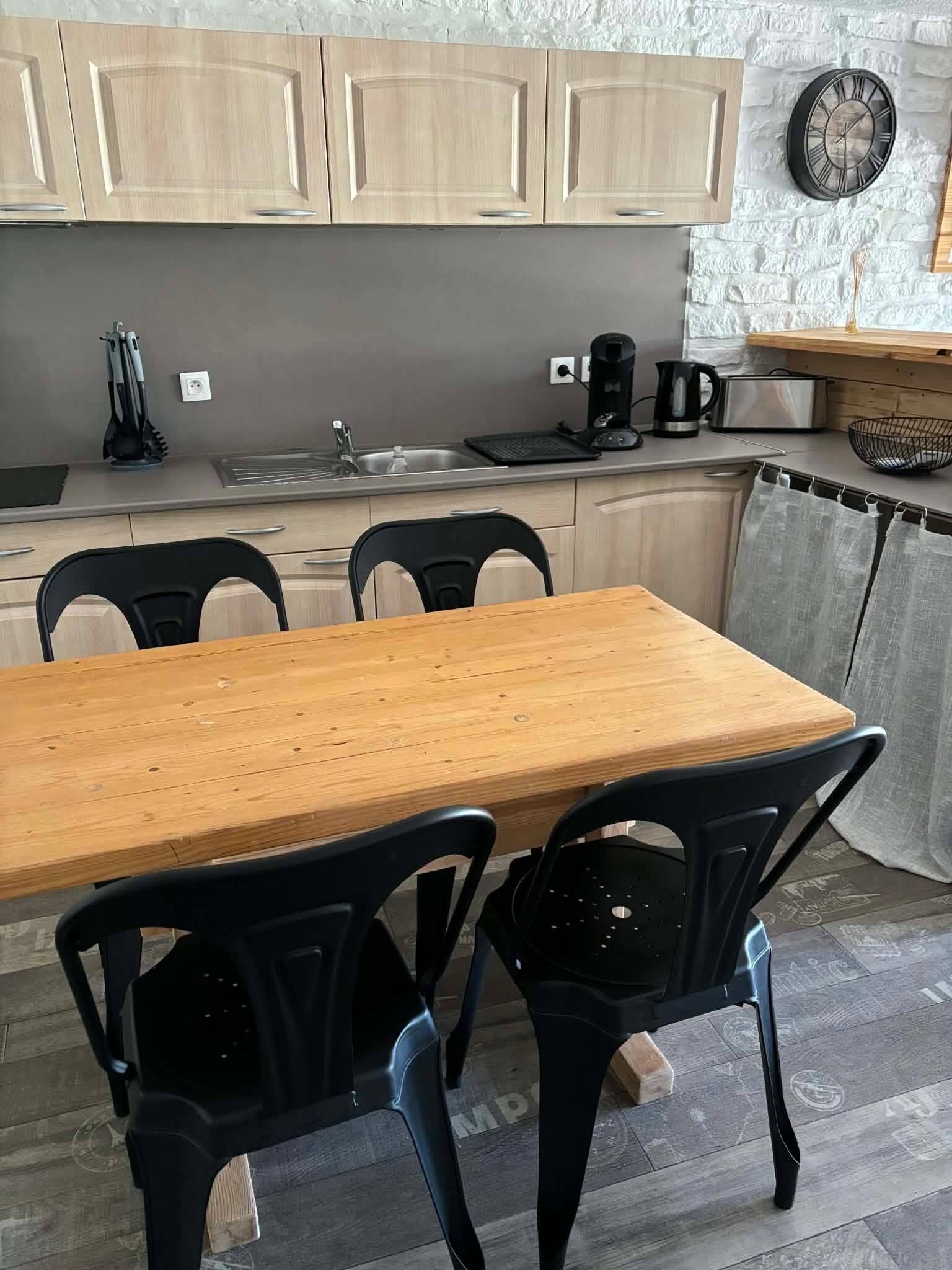 Una cocina con una mesa de madera y sillas negras, un lavabo y un reloj en la pared.