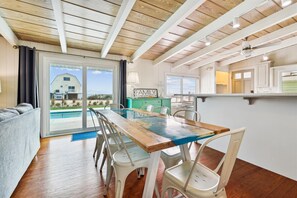 Ein geräumiges Wohnzimmer mit einem großen Holztisch und Stühlen, einer Couch und Blick auf einen Swimmingpool und ein Haus.