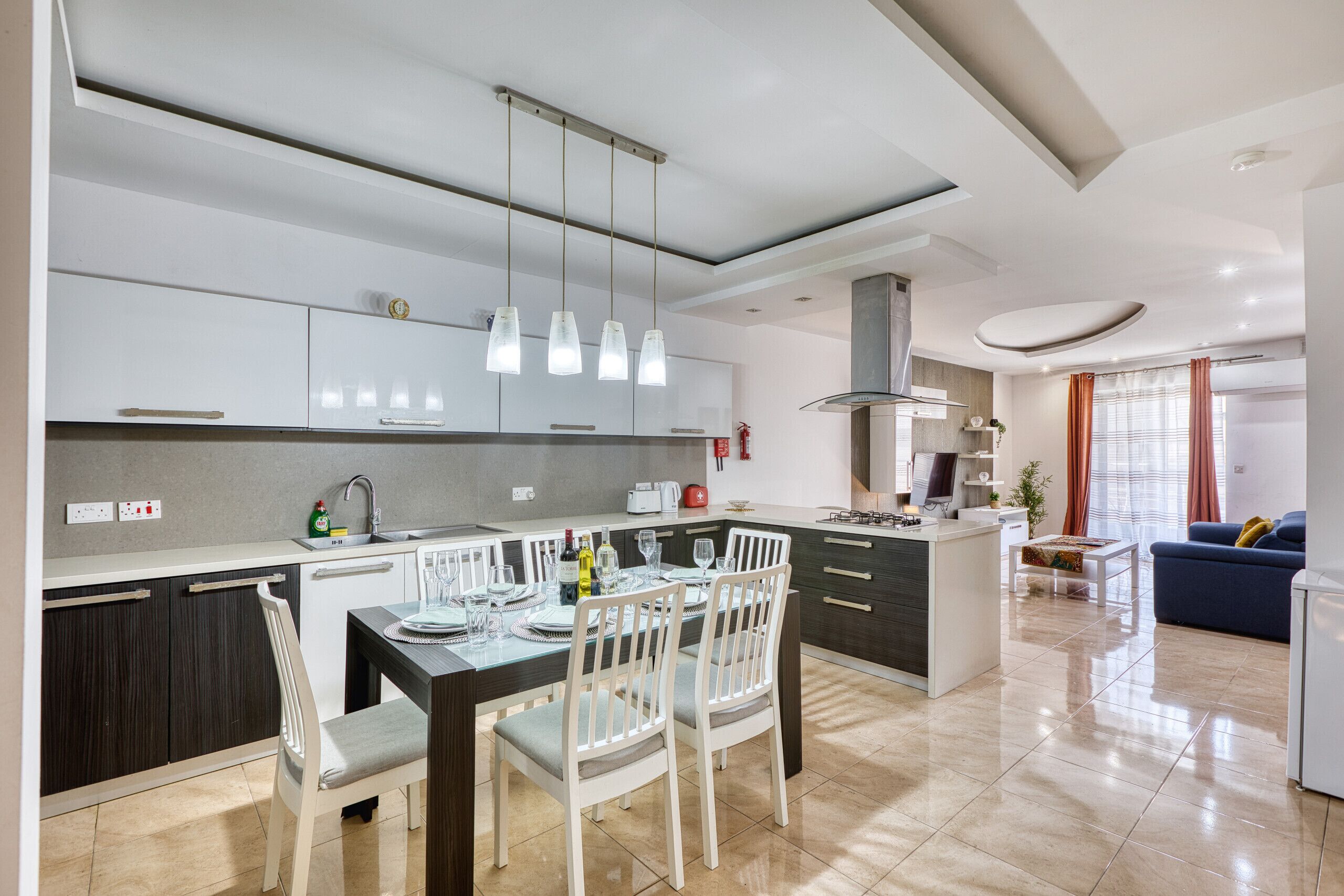 Een moderne keuken met een eethoek, een inbouweiland en een zithoek met een bank en een televisie.