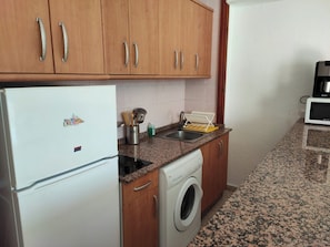 Eine kleine Küche mit Holzausstattung, einem weißen Kühlschrank, einer Waschmaschine, einer Mikrowelle und Granit Arbeitsplatten.
