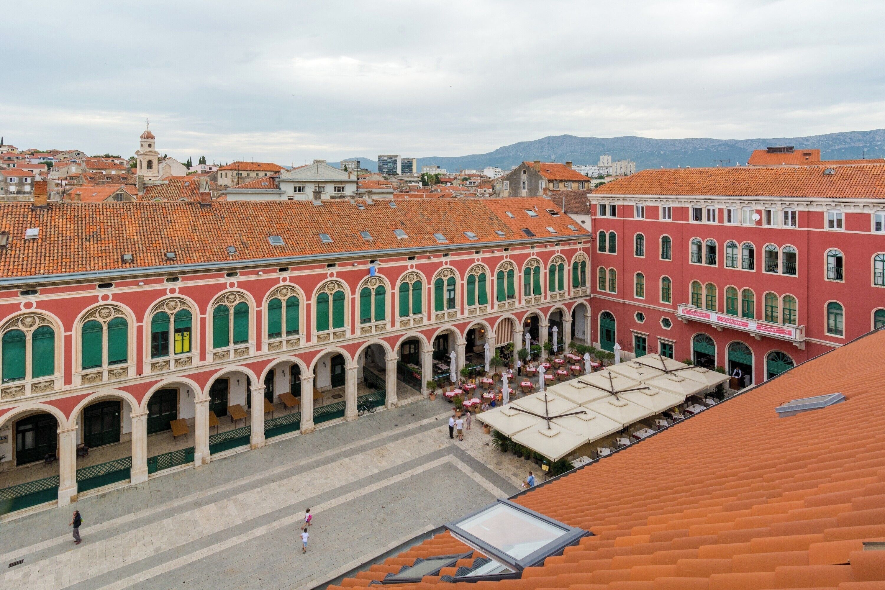 A courtyard with red-roofed buildings, a central open space, and a small fountain.