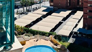 Un edificio de gran altura con zona de piscina, que incluye piscina y tumbonas, rodeado de otros edificios y una vista despejada del mar.