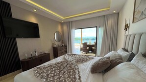 Una camera d'albergo moderna con un letto grande, una TV a parete, un comò e vista sull'oceano attraverso le porte del balcone.