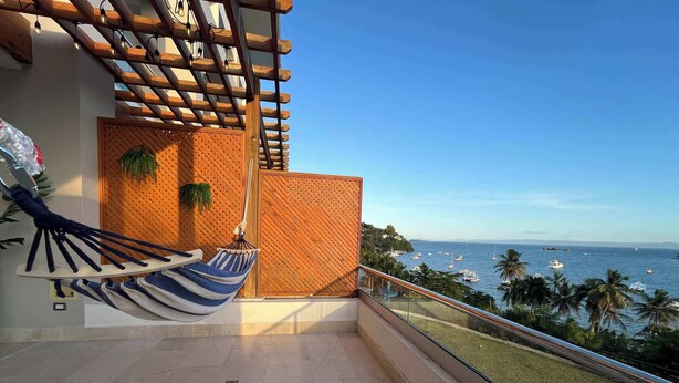 Un balcone con una poltrona a dondolo, un pergolato in legno e vista sul mare.