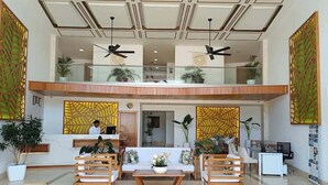 Un'ampia hall con reception, zona salotto, ventilatori a soffitto e pannelli decorativi.