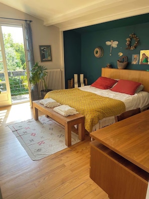 A bedroom with a bed, a bench, a wooden table, a radiator, and a view of greenery outside. - La Famille Maison Piscine Toulouse Centre (Toulouse)