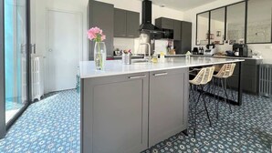 A modern kitchen with grey cabinets, a central island, and a dining area with wicker chairs. - La Conviviale - Maison Familiale Avec Piscine (Toulouse)