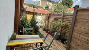 Um deck de madeira com mesa e cadeiras, cercado por um muro de madeira e plantas em vasos.