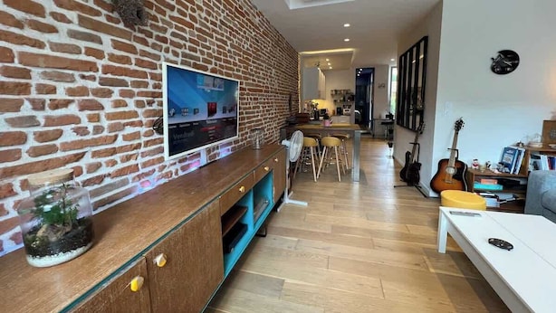 Uma sala de estar com parede de tijolos, uma televisão, um violão e um espaço para refeições.