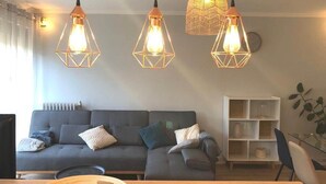 A modern living room with a sofa, a dining table, and pendant lights. - Colocation Meubl e Ar nes Bail Individuel (Toulouse)
