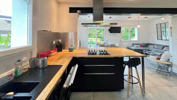 A modern kitchen with a central island, a dining area, and a living space with a sofa and TV. - L Escapade 6p Maison Familiale Jardin Piscine (Boussens)
