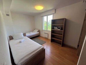 A room with two beds, a window, a radiator, and a bookshelf. - La Villa du Cedre - 6p - Proche Caliceo (Montrabe)