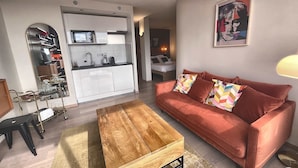 A modern living room with a red sofa, a wooden coffee table, and a kitchen area with white cabinets and a microwave. - The Manhattan - 2p- Over Toulouse s Roofs (Toulouse)