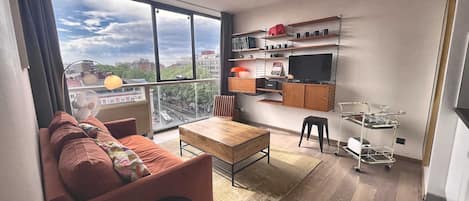 Una sala de estar moderna con un sofá, una mesa de centro, un televisor y un comedor con una mesa pequeña y sillas.