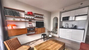 A modern living room with a wooden coffee table, a leather chair, a TV, and a kitchen area with white cabinets and a microwave. - The Manhattan - 2p- Over Toulouse s Roofs (Toulouse)