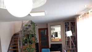 En matplats med ett träbord, stolar, en trappa, en bokhylla och en hängande lampa.
