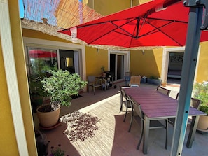 Une terrasse extérieure avec un parasol rouge, une table en bois, des chaises et des plantes en pot.