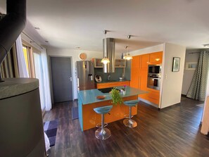 Een moderne keuken met een centraal eiland, roestvrijstalen apparatuur en oranje kastjes.