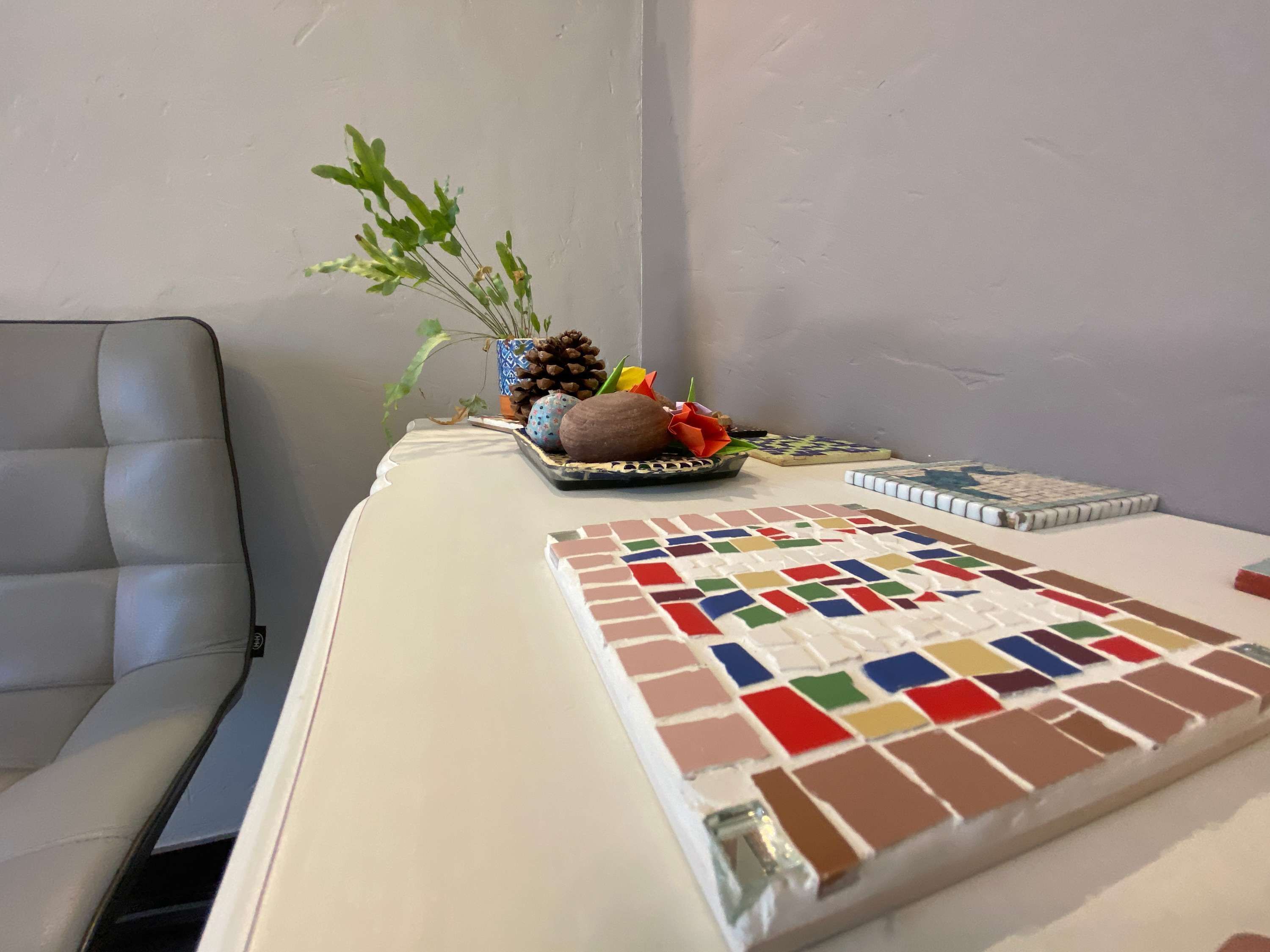 A room with a white sofa, a small table with a decorative tray, a potted plant, and a tiled area.