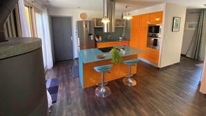 Ett modernt kök med en central köksö, rostfria vitvaror och orange köksinredning.