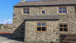 A stone building with three windows, a satellite dish, and a chimney. - 1 Upper Austby Farm Cottage (Ilkley)