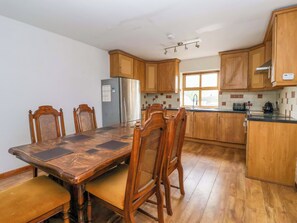 A kitchen with wooden cabinets, a stainless steel refrigerator, a dining table with chairs, and a window providing natural light. - 1 Upper Austby Farm Cottage (Ilkley)