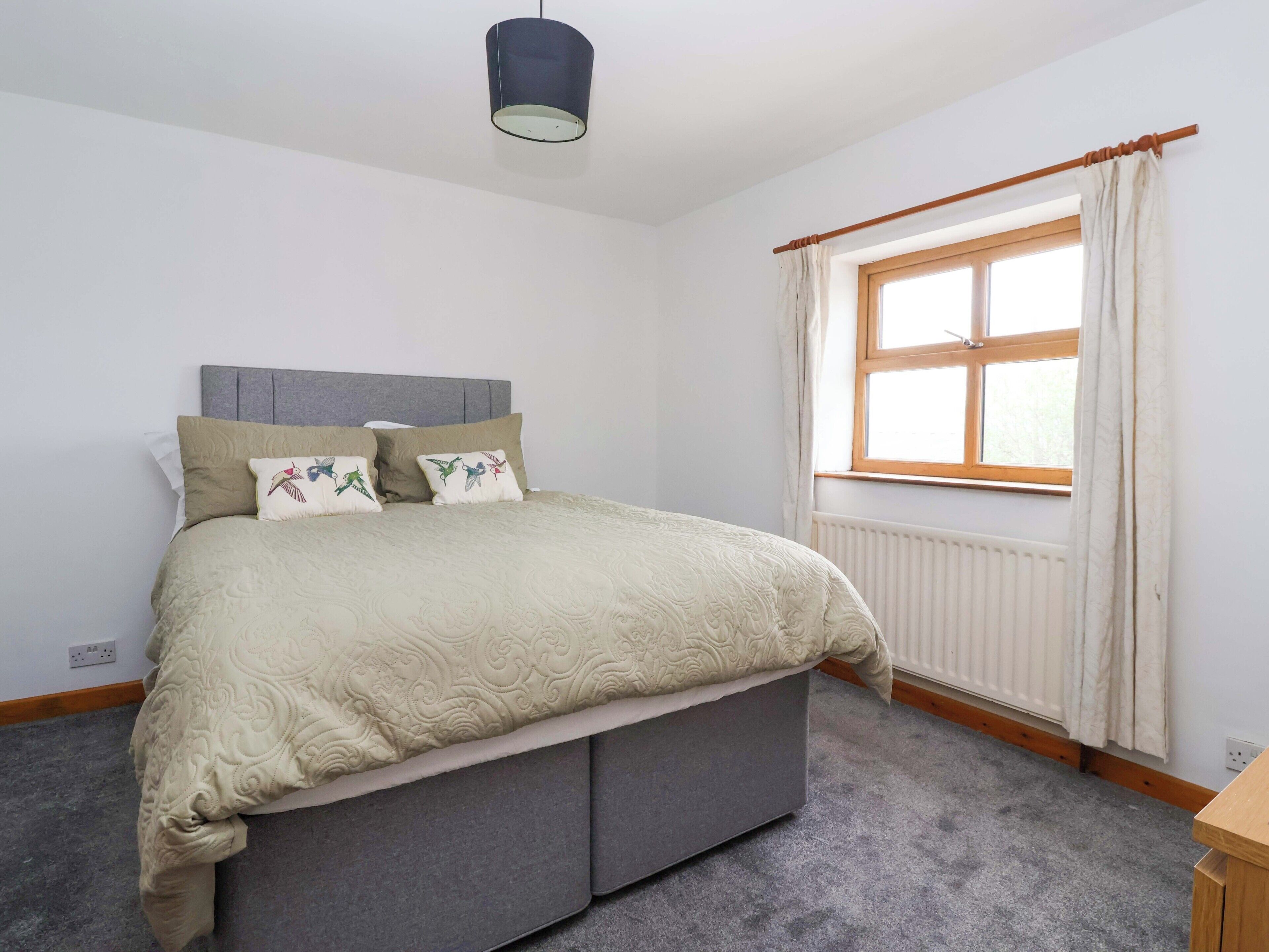 A bedroom with a bed, a window with curtains, a radiator, and a ceiling light.