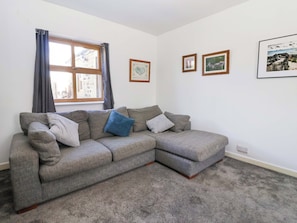 A grey sectional sofa with cushions, a window with curtains, and framed pictures on the wall. - 1 Upper Austby Farm Cottage (Ilkley)