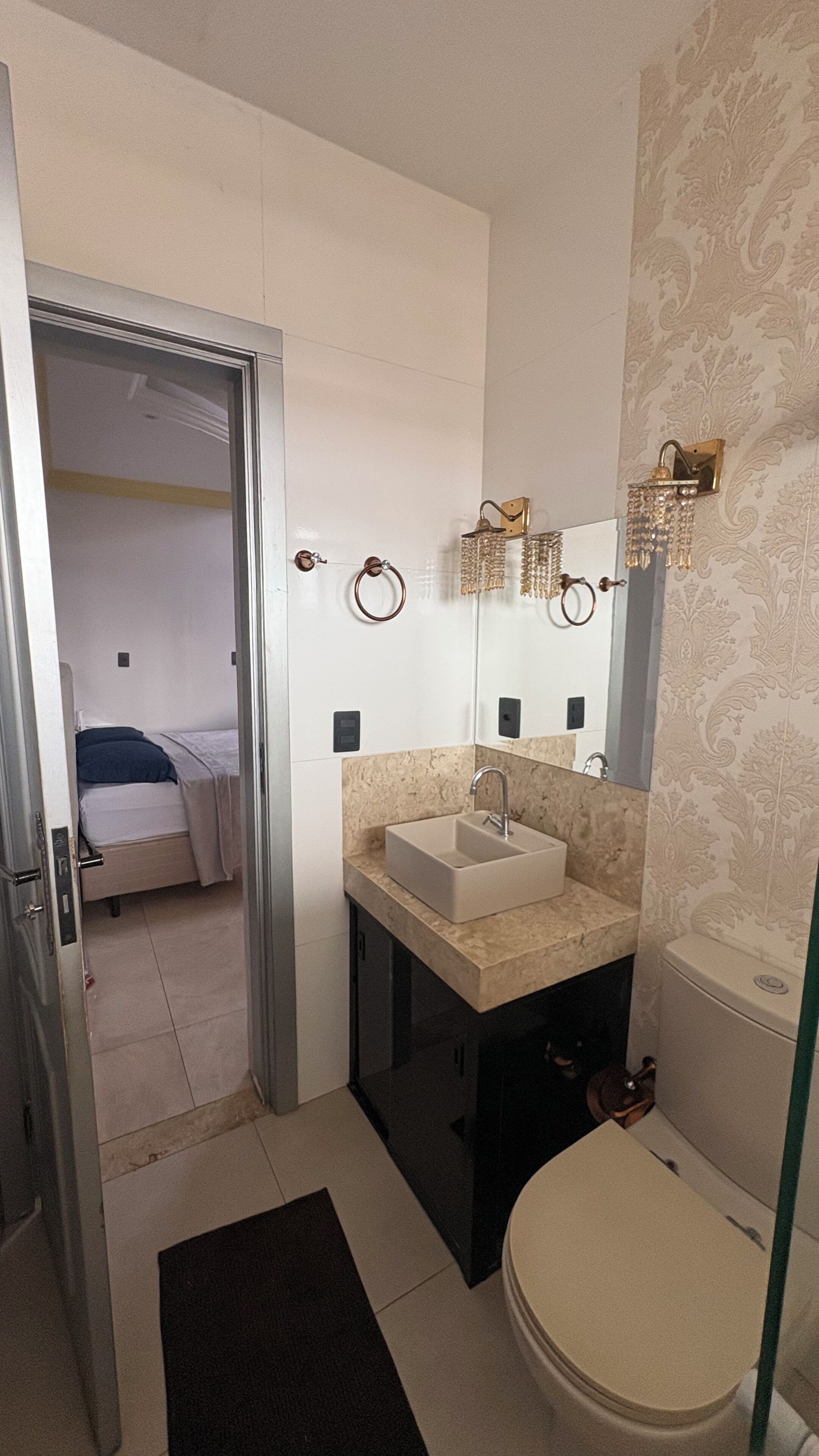 Un baño con lavamanos, espejo y retrete. Hay una puerta que da a un dormitorio.
