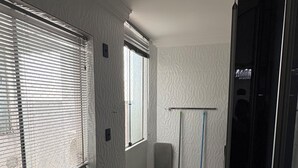 Una cocina compacta con horno integrado, una ventana con persianas, una puerta que da a otra habitación y suelo de baldosas.