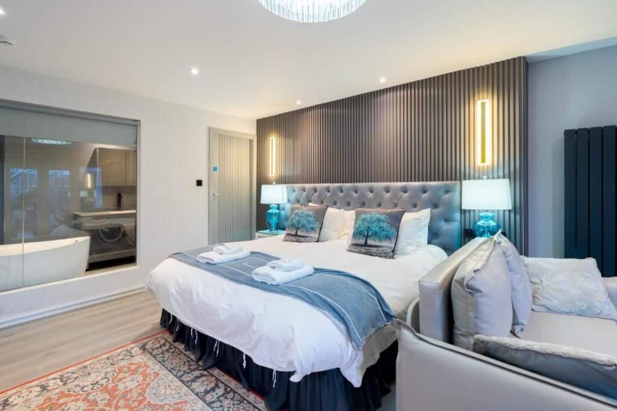 Una habitación de hotel moderna con una cama grande, un área de descanso, un baño con bañera y un espejo amplio.