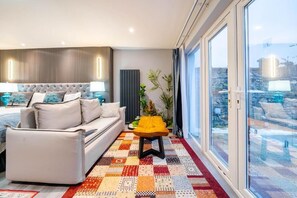 A modern bedroom with a large bed, a sofa, a small table, and a view through a glass door. - Waterhead Bath Suites (Ambleside)