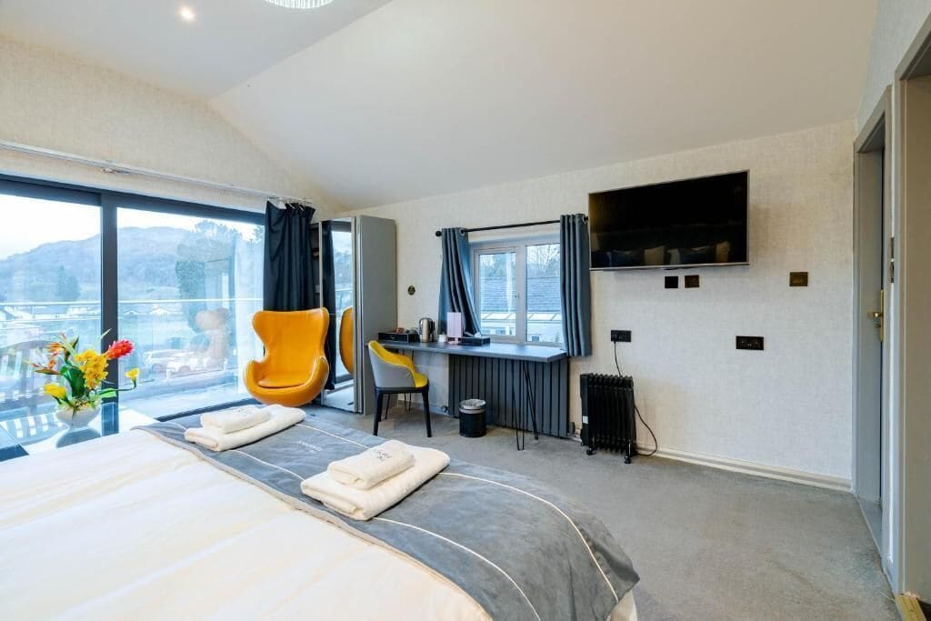 A modern hotel room with a large bed, a desk, a chair, a TV, and a view of the outdoors.