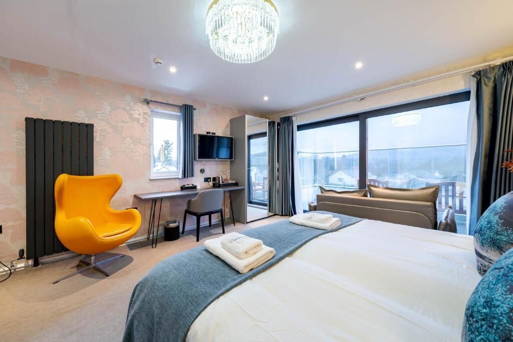 A hotel room with a large bed, a desk, a chair, a television, and a view of the city.