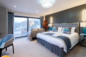 A modern hotel room with a large bed, a seating area, and a view of the outdoors. - Waterhead Bath Suites (Ambleside)