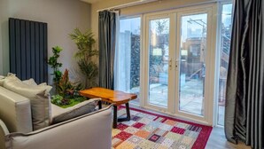 Un salon avec un canapé, une petite table, une plante en pot et une vue à travers une porte vitrée.