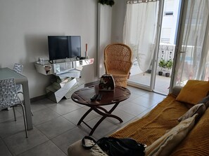 A living room with a TV, a sofa, a chair, a small table, and a balcony with plants. - Charming apartment, Anglet (Anglet)