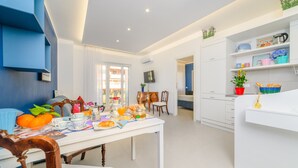 Una cocina moderna con muebles blancos, una mesa de comedor con platos y naranjas, y vista al área de comedor contigua.